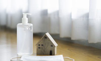 Hand sanitizer with protective mask next to small wooden model house