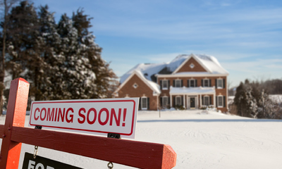 For sale sign in front of a large house on a snowy surface