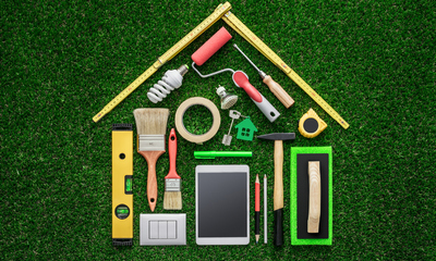 Home renovation tools laid out on a grass surface to create a shape of a house