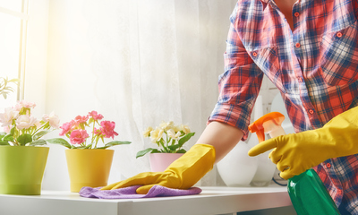 A pair of hands wearing rubber gloves, wiping tabletop with a cloth and holding a spray bottle