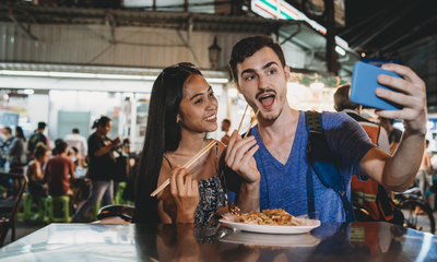 Young couple having dinner together together at the night market taking a selfie